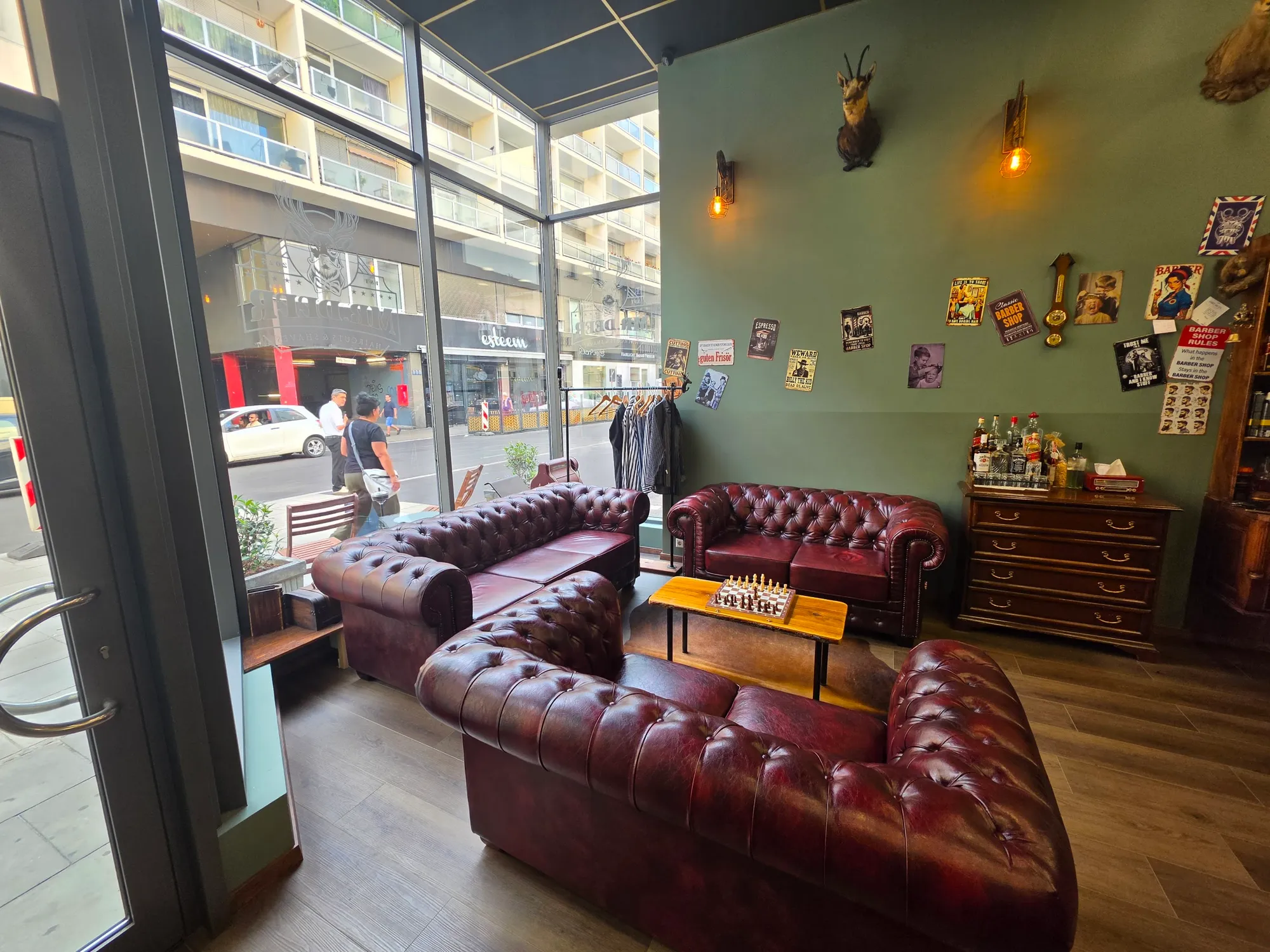 Lounge mit dunkelroten Chesterfield-Sofas, Schachbrett, salbeigrüner Wand mit Geweihen und Blechschildern