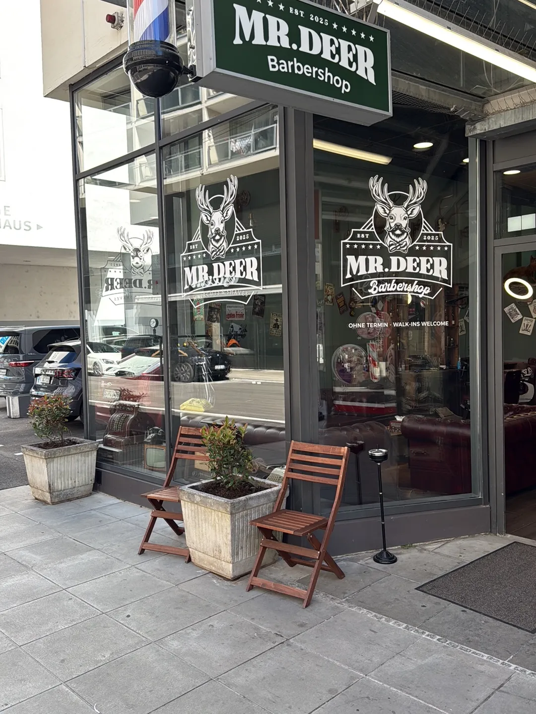 Ladenfront von MR DEER mit grünem Schild „MR.DEER Barbershop, Est. 2025“ und dem Hirsch-Logo auf der Scheibe